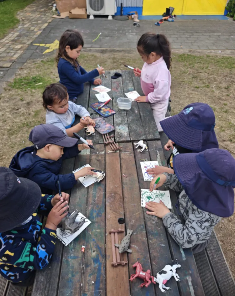Tamariki drawing and painting together around the outdoor picnic table