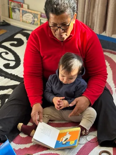 A kaiako sharing a picture book with pēpi on the mat