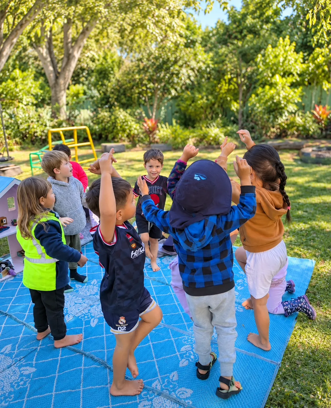 Tamariki stretching and singing together in a circle outside in the sunshine