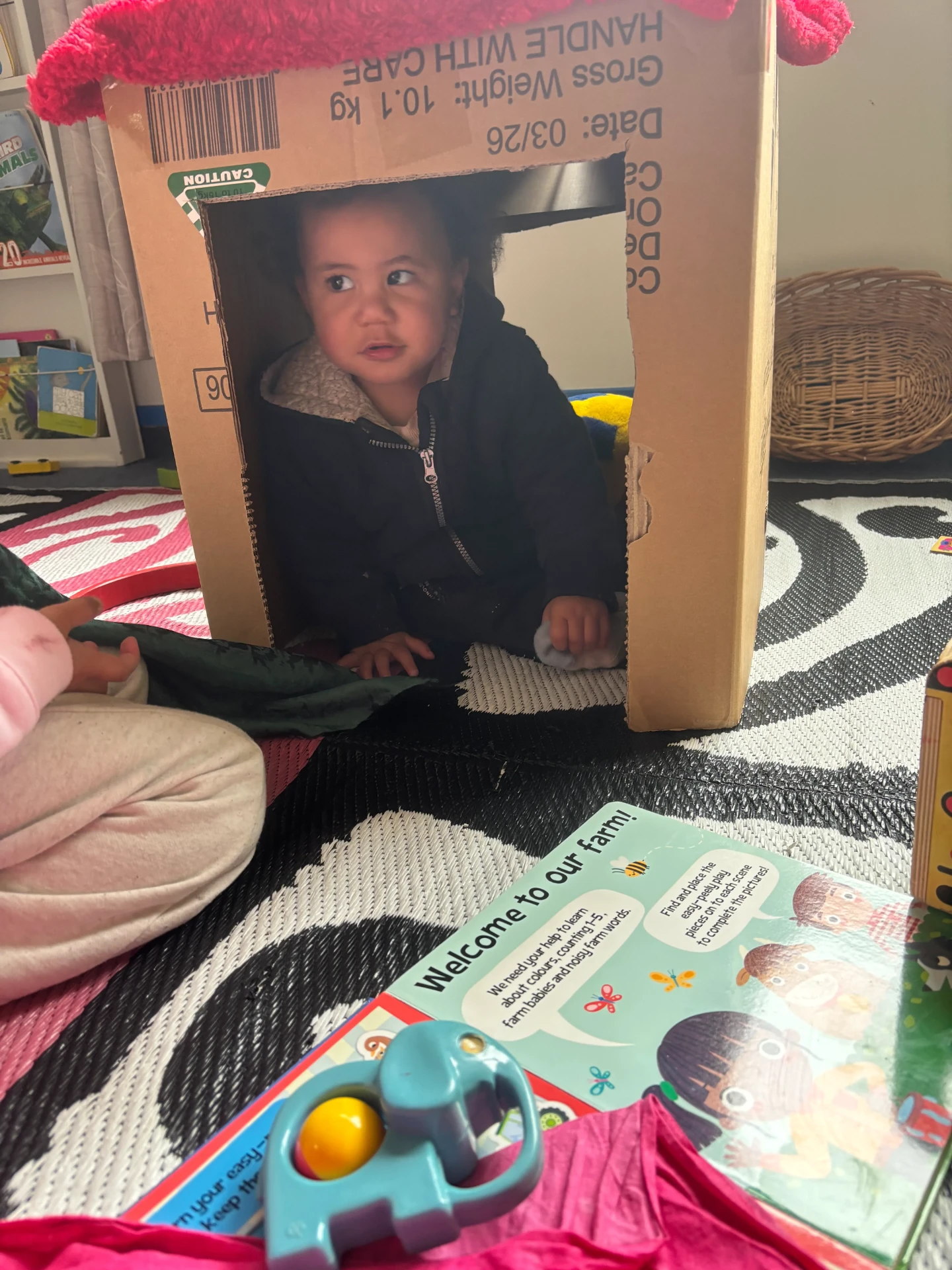 A pēpi peeking out of a cardboard box hut in the under 2 room at Little Darlings Childcare in Rotorua